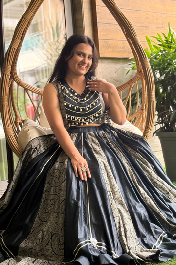 The sleek black choli is adorned with mirror embellishments and golden piping